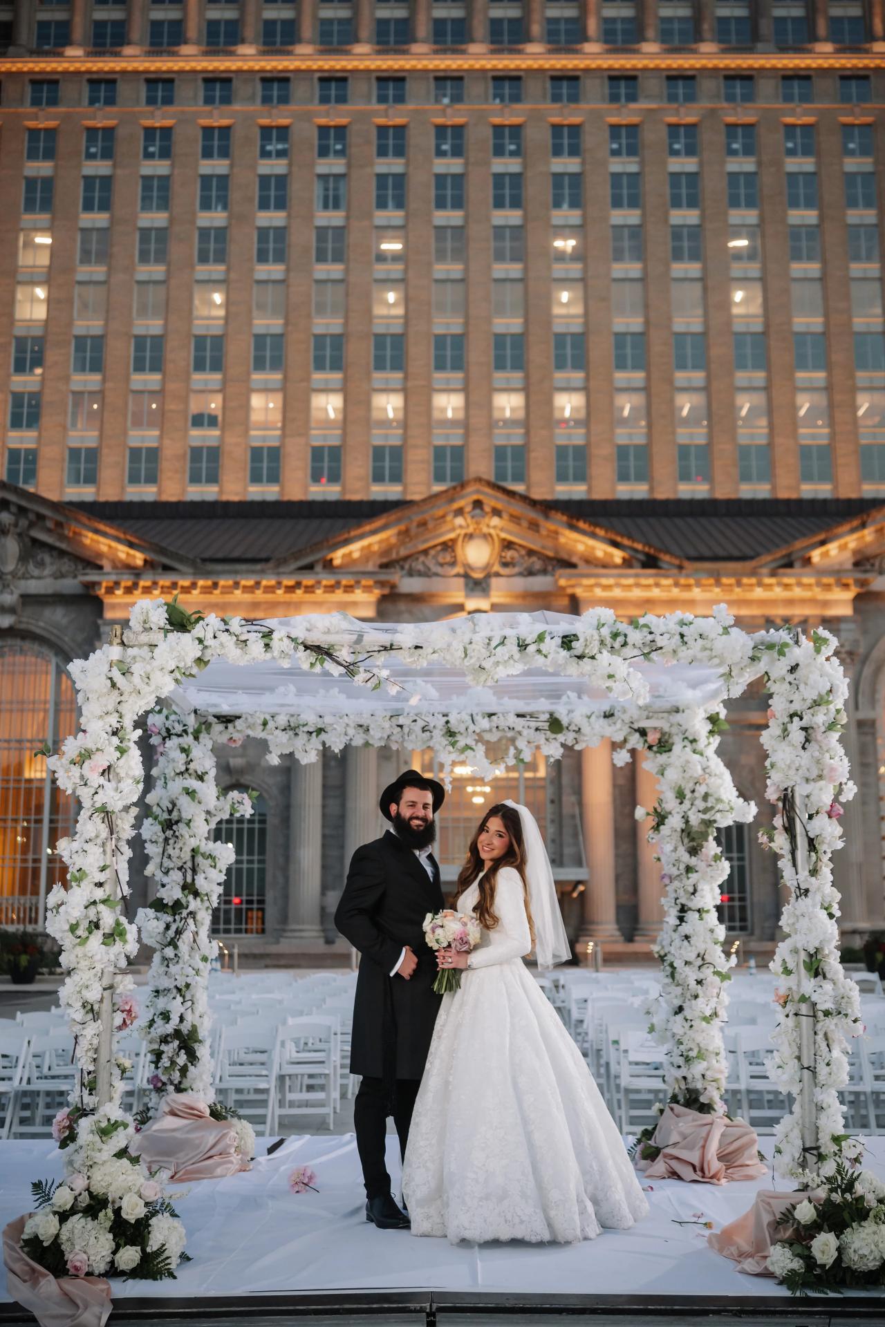 Bride and groom beneath the floral chuppah at twilight. Jewish wedding in Detroit.