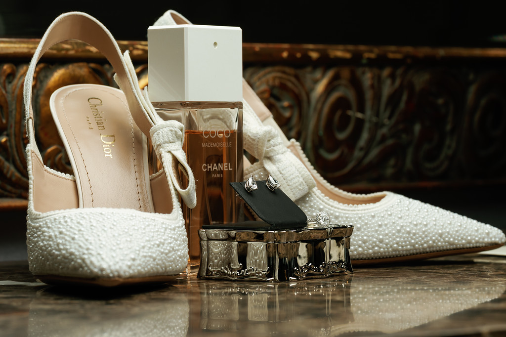 Close-up flat-lay of bridal heels and accessories, including pearl embellished shoes and a perfume box, arranged on a mirrored surface.