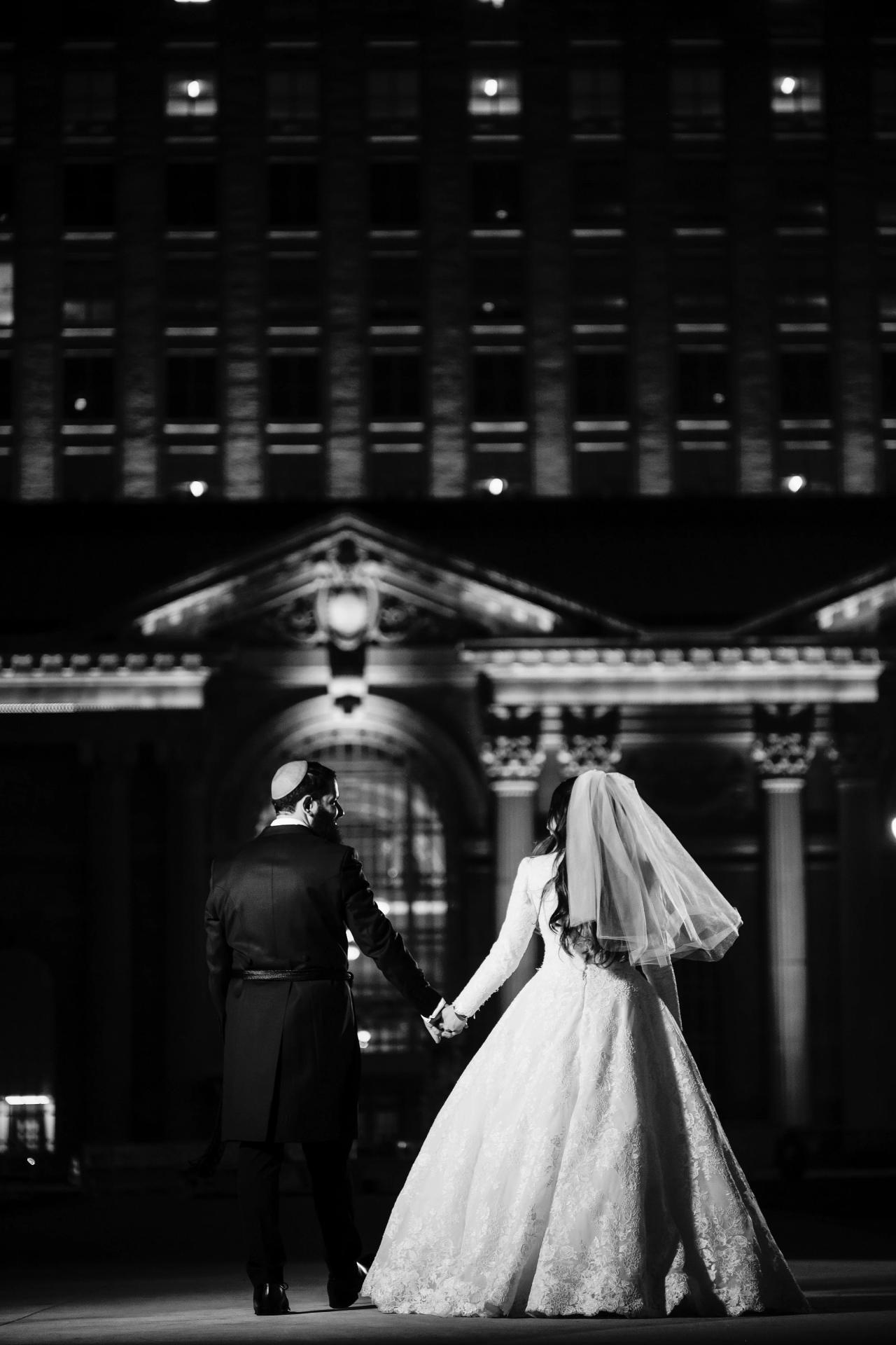 Black-and-white wedding portrait outside the illuminated venue. Jewish wedding in Detroit.
