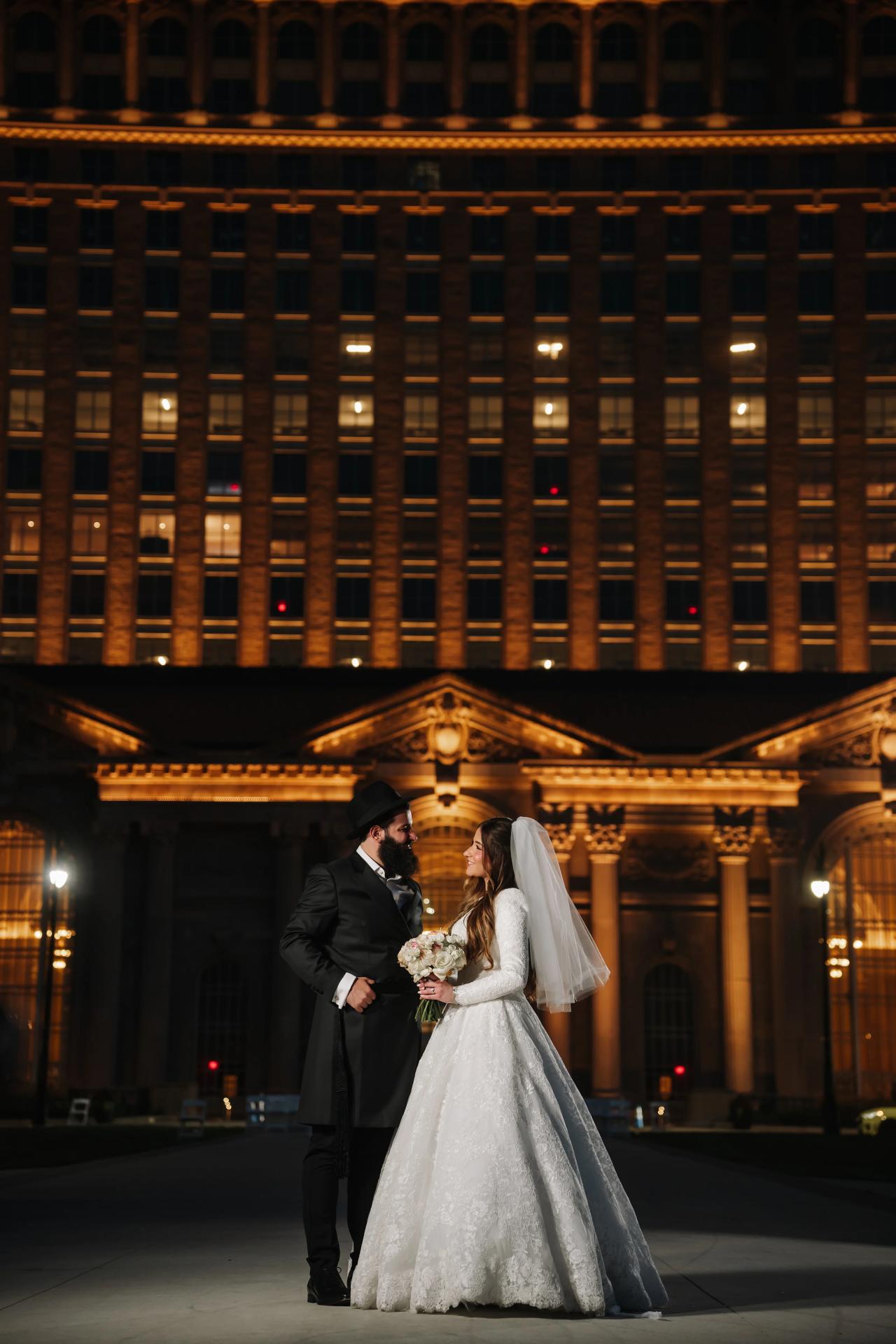 Bride and groom sharing a nighttime portrait beneath warm architectural lights. Jewish wedding in Detroit.