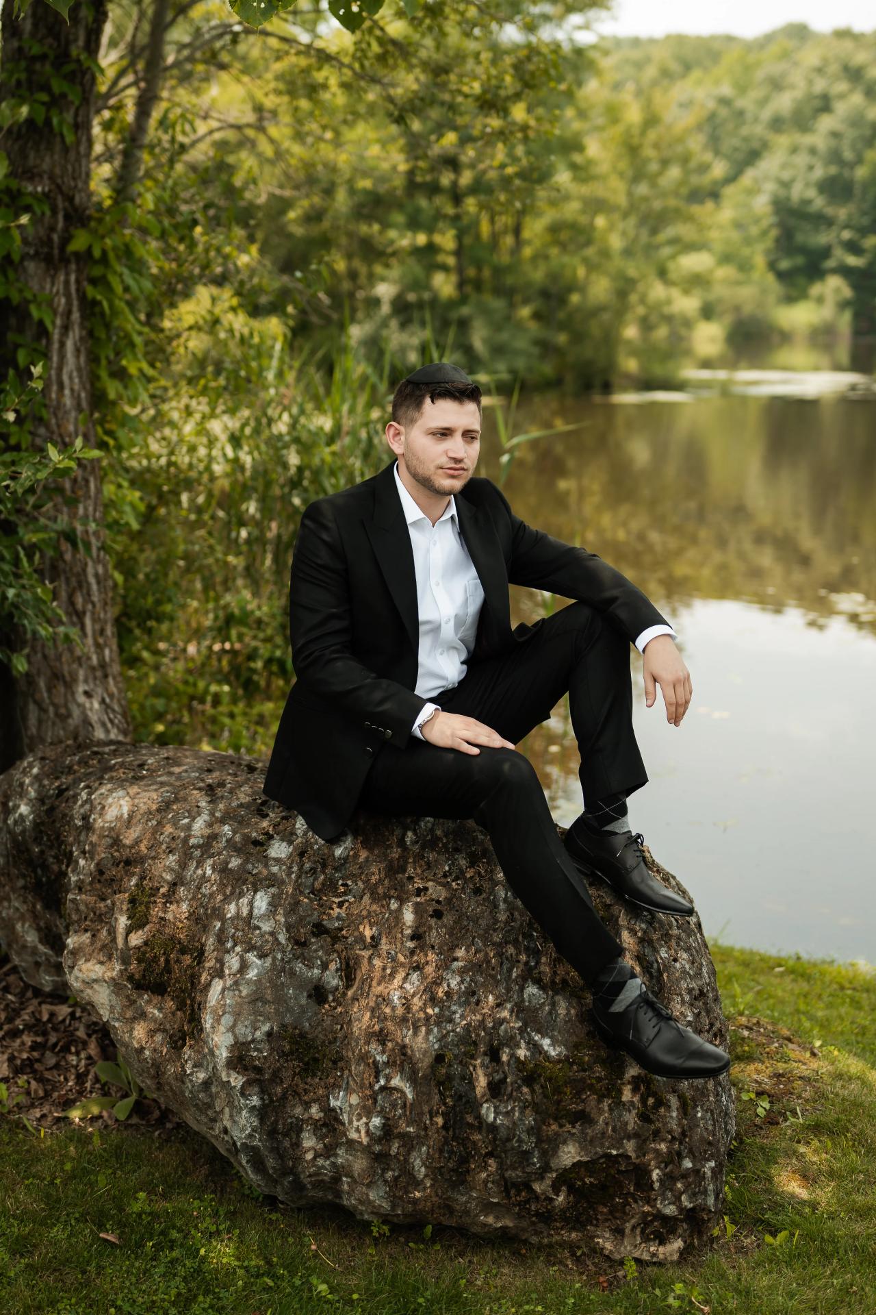 Groom seated on a rock beside the lake. Wedding at Indian Ridge.