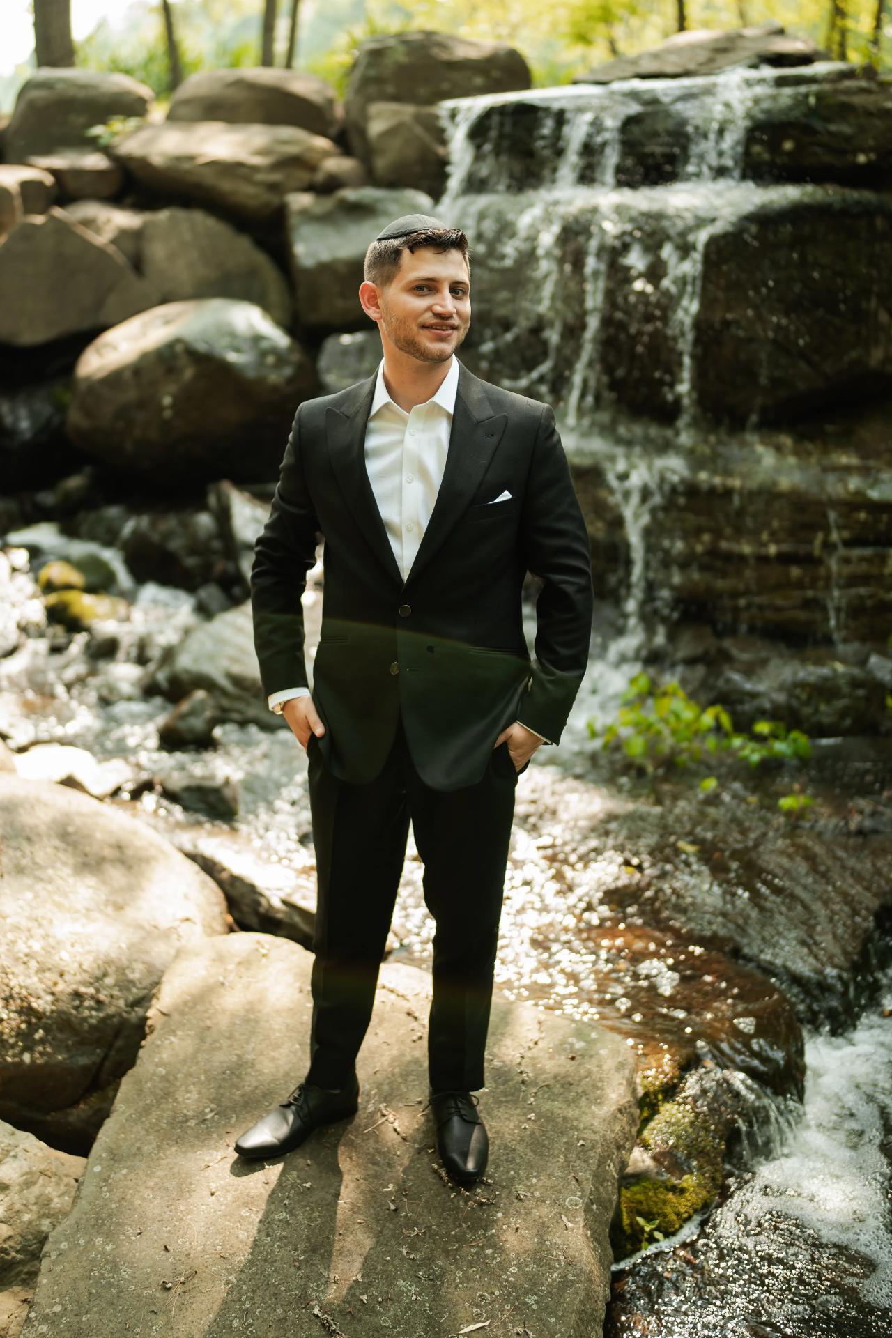 Groom standing beside the garden waterfall. Wedding at Indian Ridge.