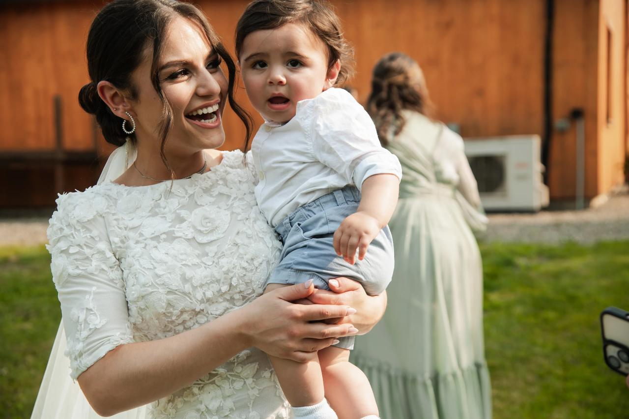 Bride smiling while holding a young wedding guest. Wedding at Indian Ridge.