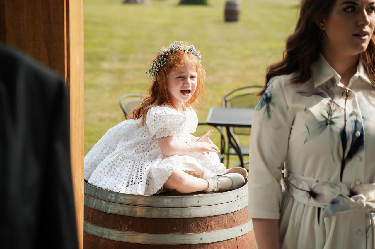 Flower girl seated beside the rustic barn. Wedding at Indian Ridge.