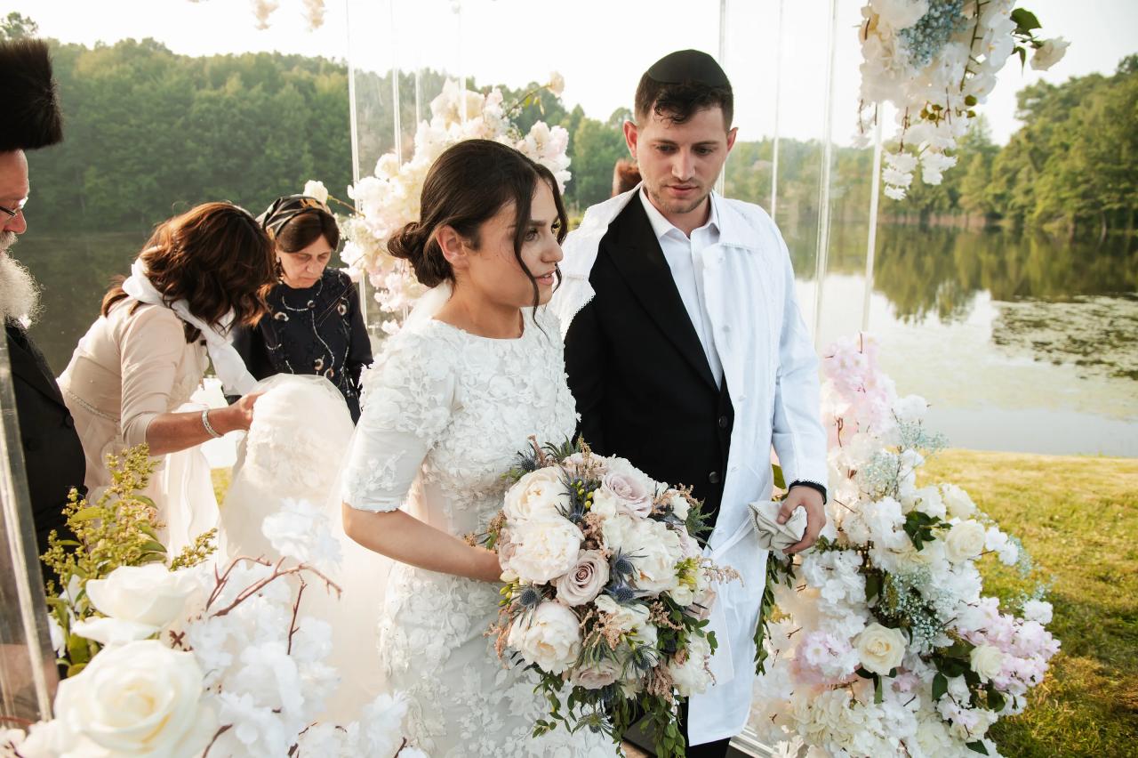 Bride and groom standing beside their flower-covered chuppah. Wedding at Indian Ridge.