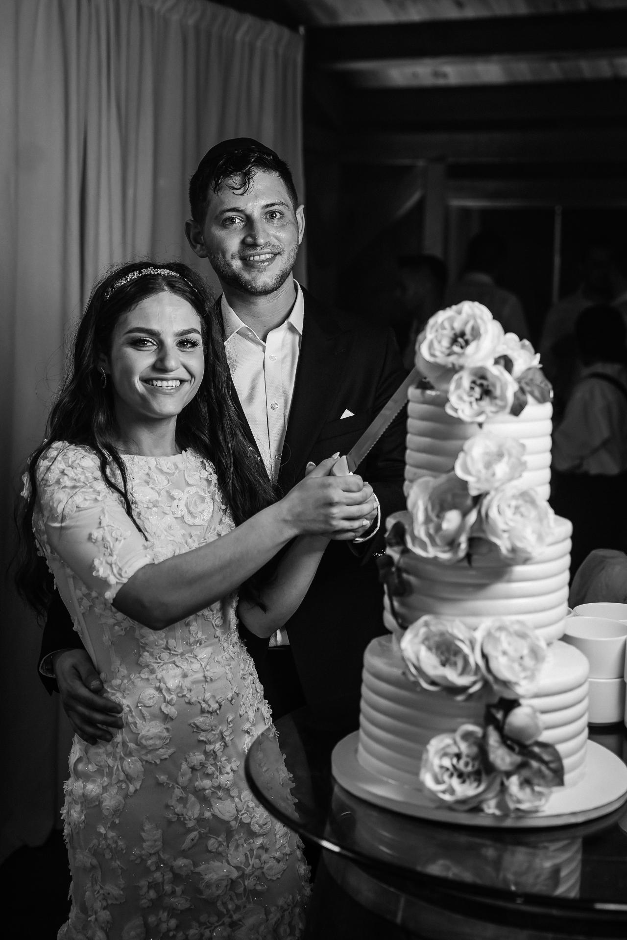 Black-and-white wedding couple beside their floral wedding cake. Wedding at Indian Ridge.