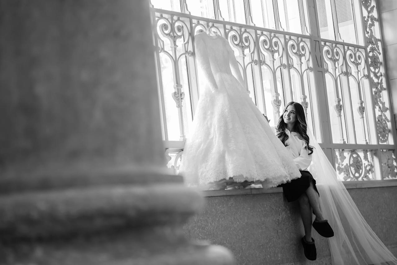 Black-and-white bride beside her hanging wedding dress, framed by a stone column in Detroit