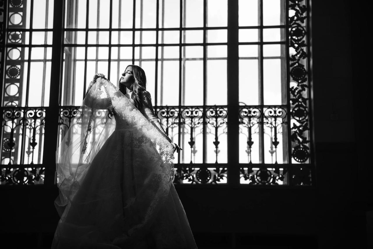 Bride silhouetted with her embroidered veil against a tall ornate window in Detroit