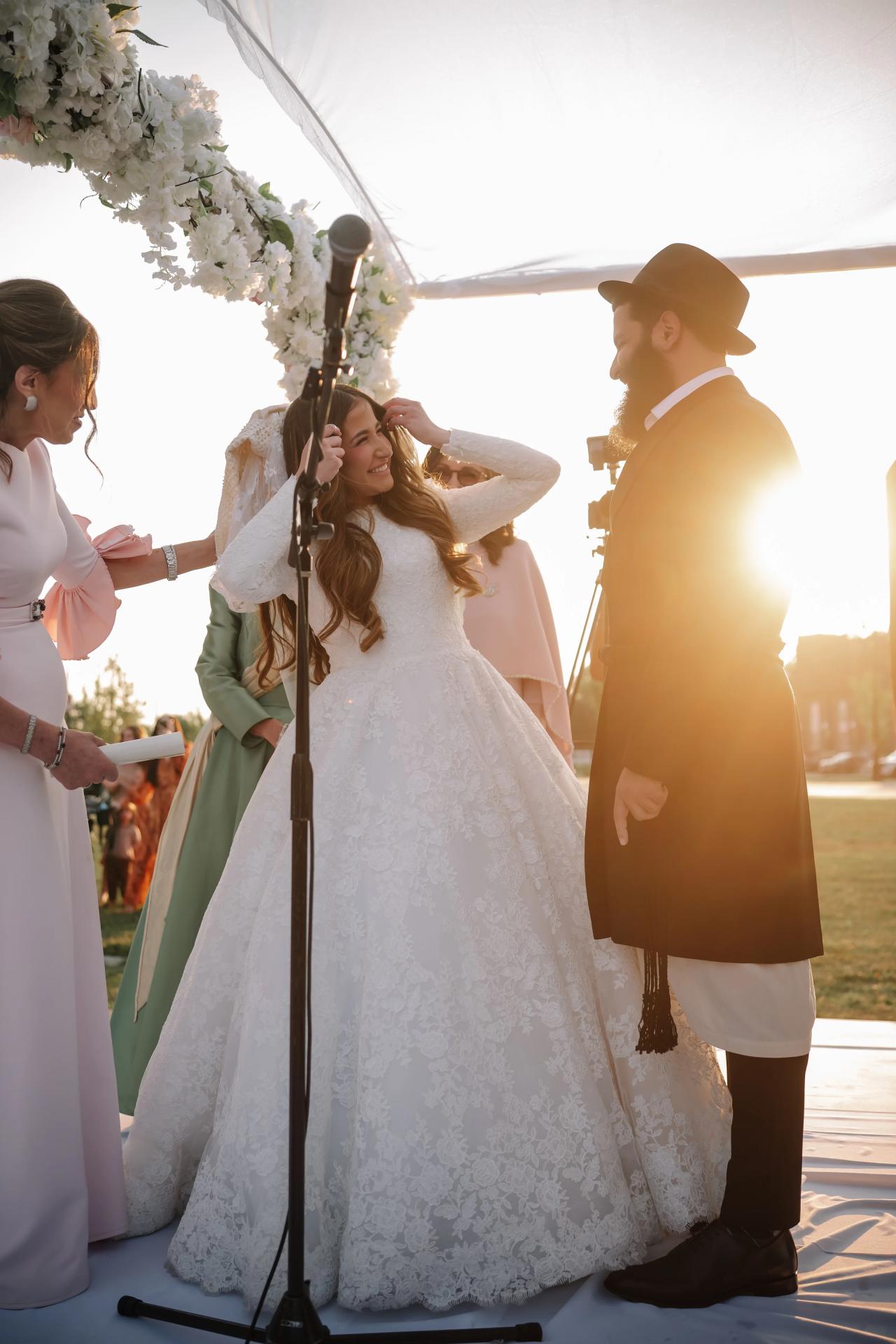 Bride and groom beneath the floral chuppah with sunlight glowing behind them in Detroit