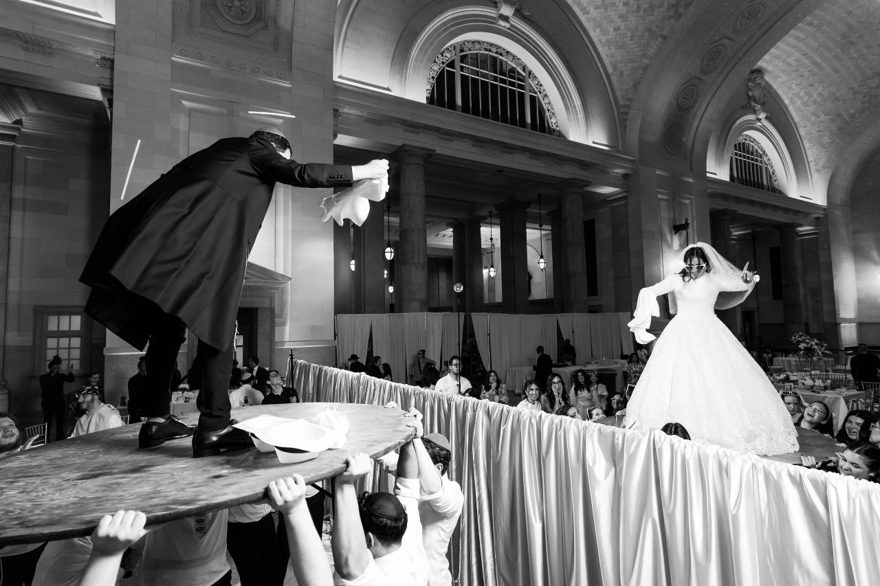 Black-and-white bride and groom lifted above guests beneath grand ballroom arches in Detroit