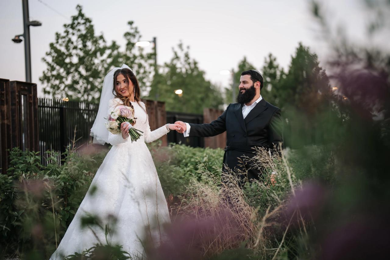 Bride and groom holding hands, framed through soft garden flowers in Detroit