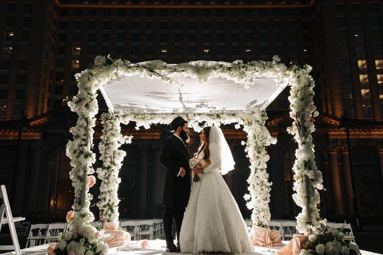 Bride and groom beneath a brightly illuminated floral chuppah at night in Detroit
