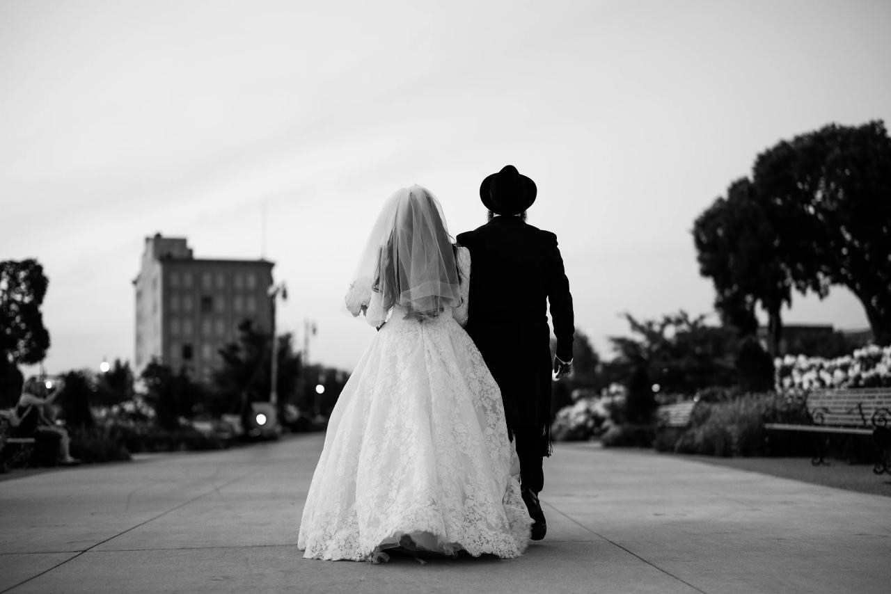 Black-and-white bride and groom walking away together along a Detroit garden path