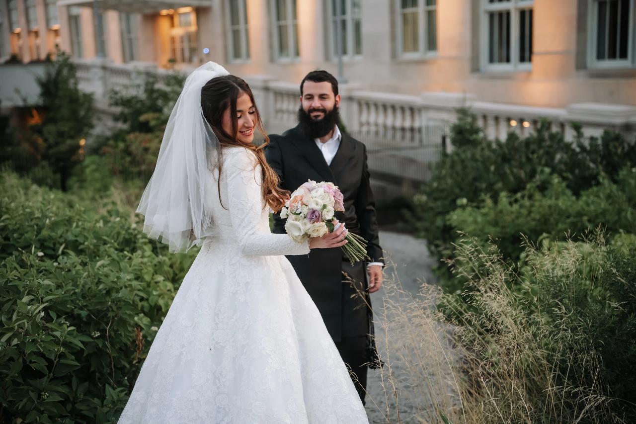 Bride looking back with the groom behind her and her veil flowing through a Detroit garden