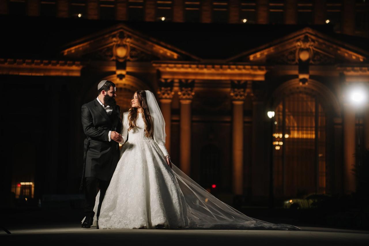 Bride and groom holding hands at night with an embroidered train across the foreground in Detroit
