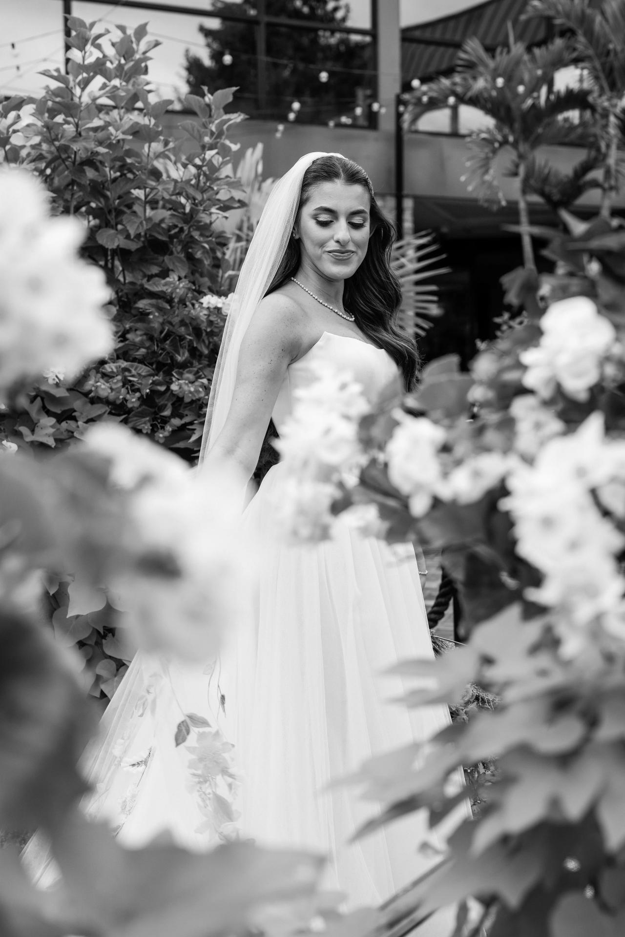 Black-and-white bride framed through soft foreground flowers in the Crest Hollow gardens, Woodbury, Long Island.