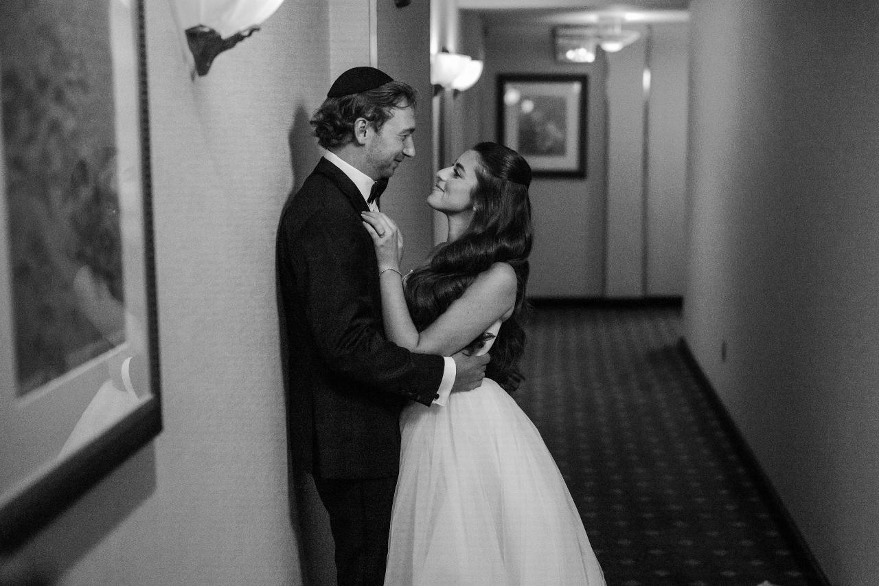 Black-and-white bride and groom embracing in a hallway with strong receding lines at Crest Hollow, Woodbury, Long Island.