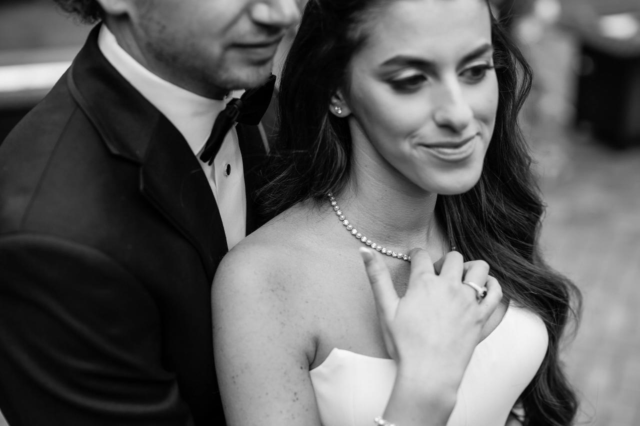 Black-and-white close bridal portrait with pearl necklace and the groom softly framed behind her at Crest Hollow, Woodbury, Long Island.