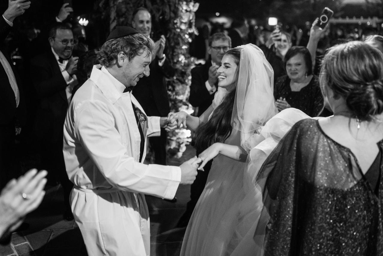 Black-and-white bride and groom smiling and holding hands during a dance after their ceremony at Crest Hollow, Woodbury, Long Island.