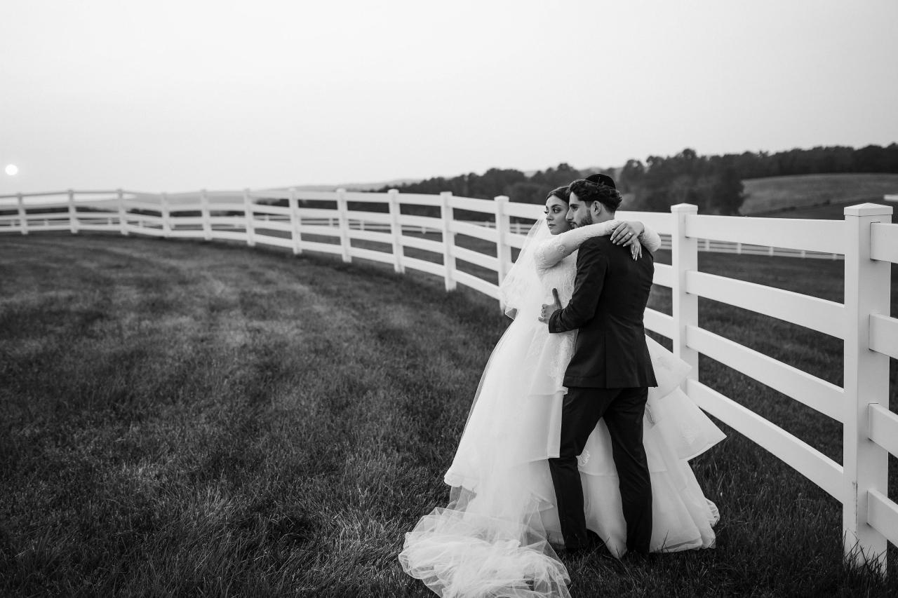 Black and white wedding portrait of the bride and groom embracing beside a curving white fence at sunset in Baltimore. Wedding photography at Vignon Manor Farm, Baltimore, MD.