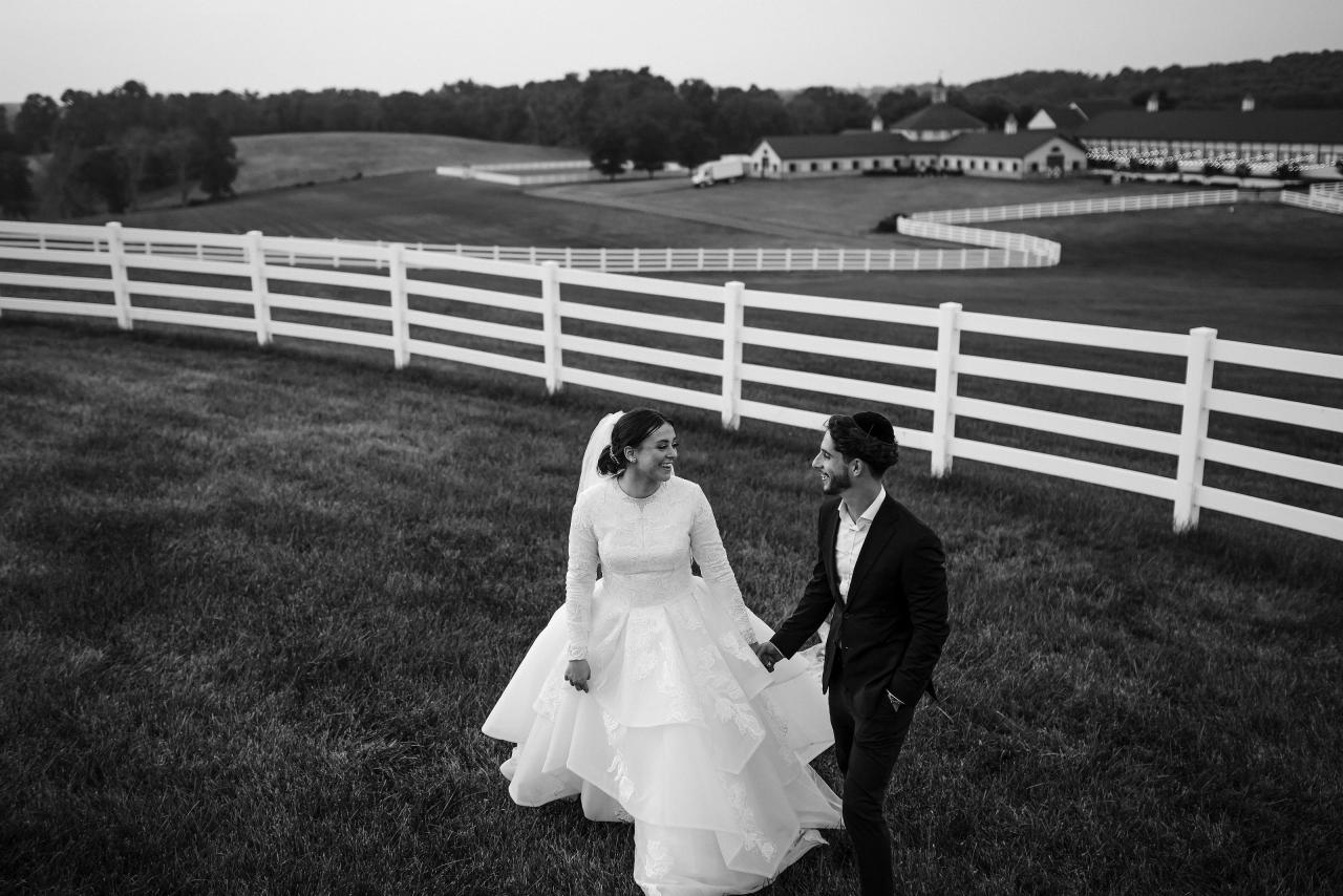 Black and white wedding portrait of the bride and groom holding hands on the lawn with sweeping countryside fences in Baltimore. Wedding photography at Vignon Manor Farm, Baltimore, MD.