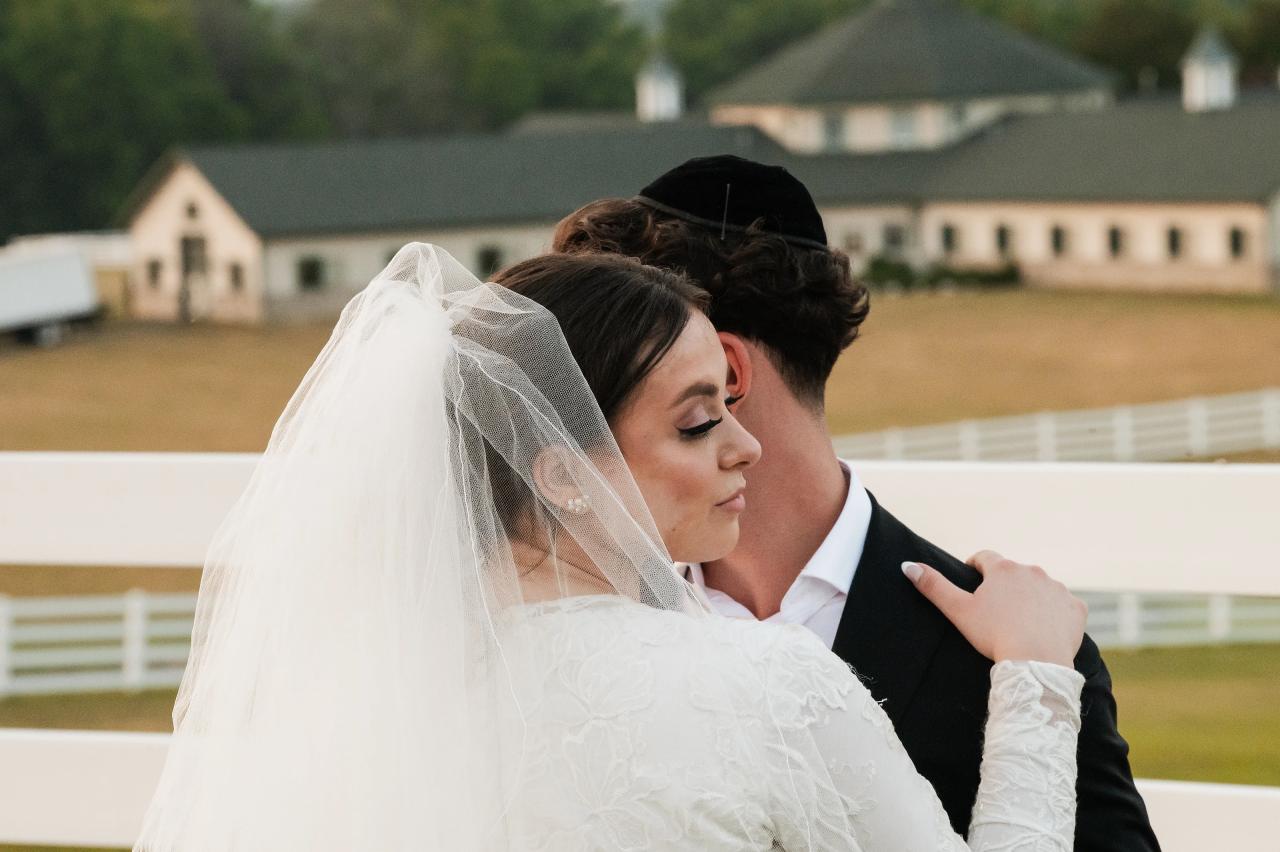 Close evening wedding portrait of the bride with eyes closed as the groom embraces her beside a white fence in Baltimore. Wedding photography at Vignon Manor Farm, Baltimore, MD.