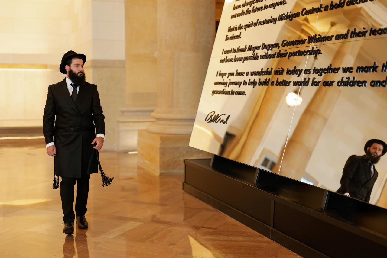 Man in formal attire walking in a warmly lit ceremony hall beside an angled program banner on a reflective floor.