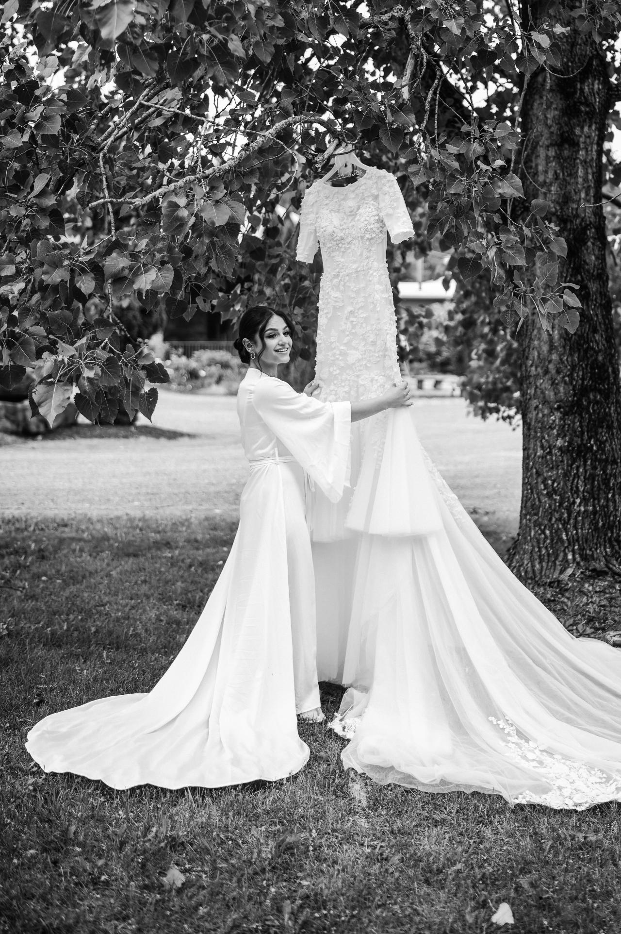 Black-and-white outdoor wedding portrait of a bride smiling mid-twirl, veil and dress flowing beneath leafy trees. Wedding photography at The Barn At Indian Ridge, Highland, NY.