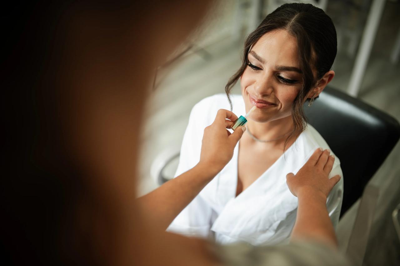 Bride smiling softly while applying makeup or adjusting her bridal look in soft indoor light, with shallow depth of field. Wedding photography at The Barn At Indian Ridge, Highland, NY.