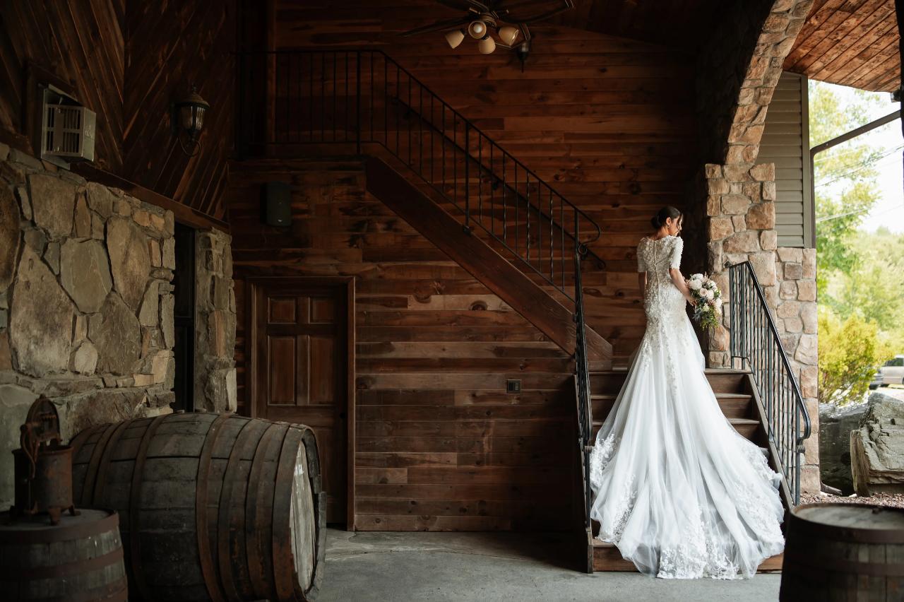 Bride walking through a rustic stone-and-wood building doorway with her wedding gown flowing in the light, staircase and barrels in the background. Wedding photography at The Barn At Indian Ridge, Highland, NY.
