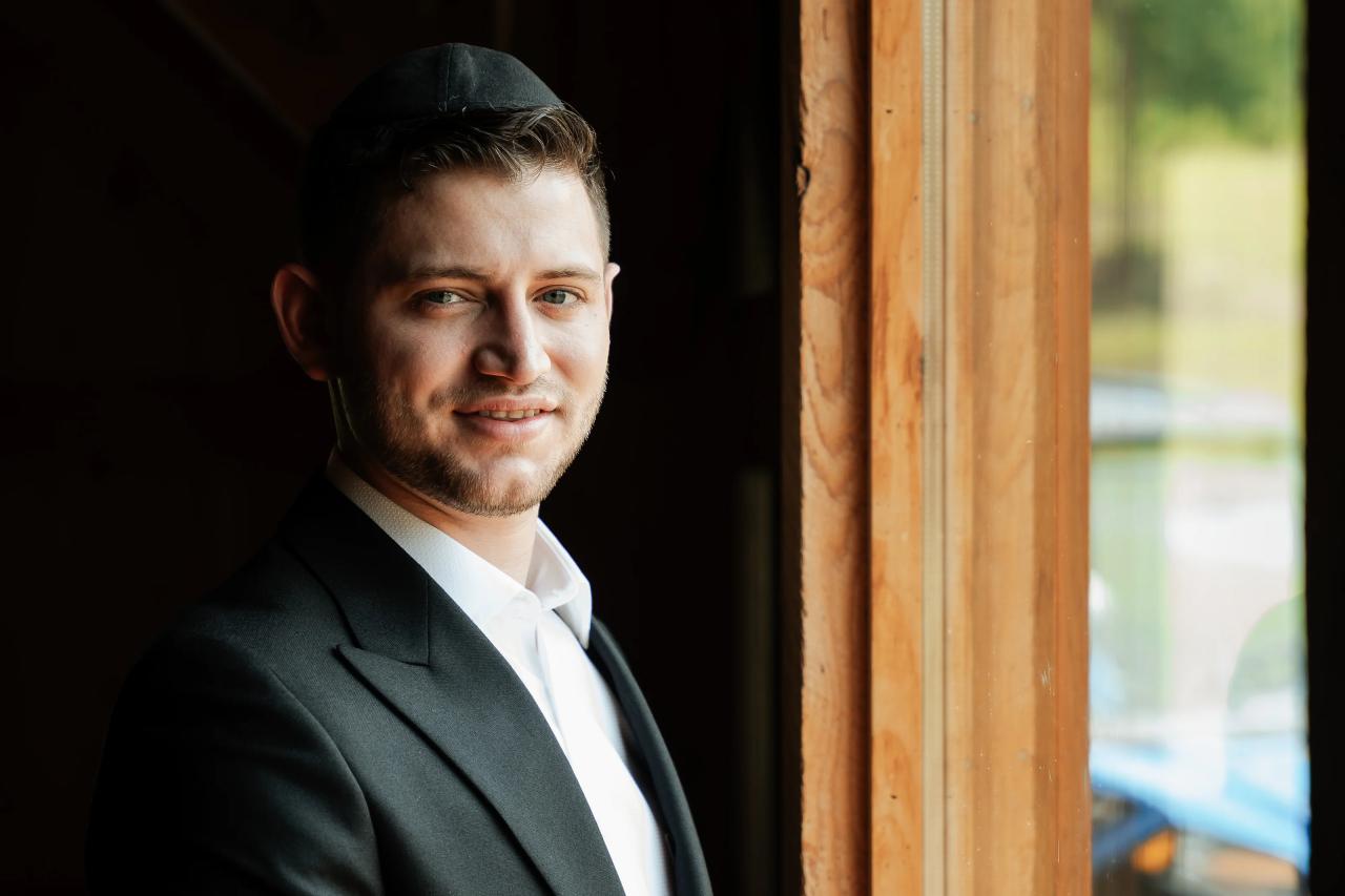 Groom in a dark suit portrait indoors with warm wood tones and dramatic shadowed lighting. Wedding photography at The Barn At Indian Ridge, Highland, NY.