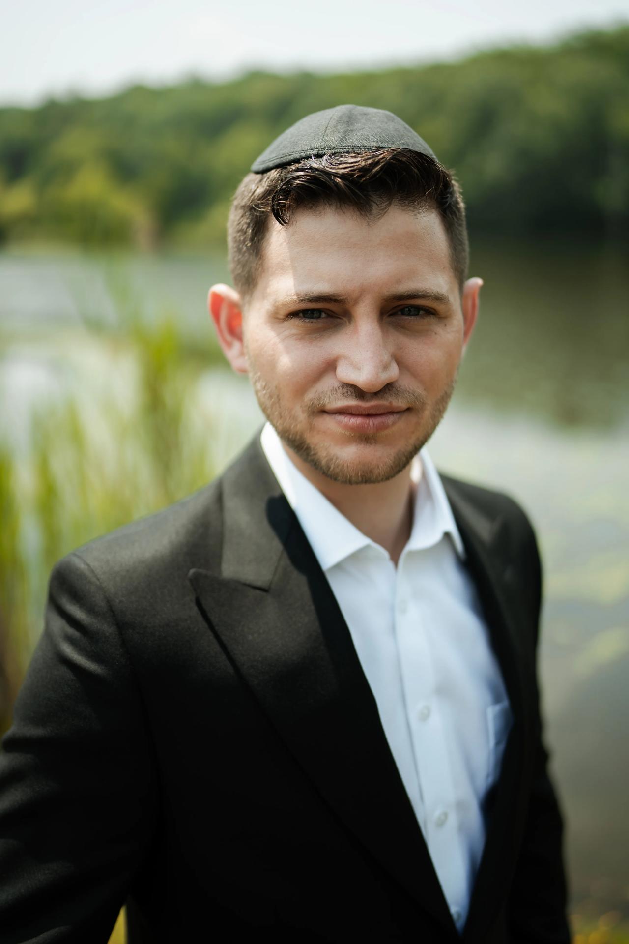 Outdoor groom portrait with kippah, shallow depth of field, and greenery background blur. Wedding photography at The Barn At Indian Ridge, Highland, NY.