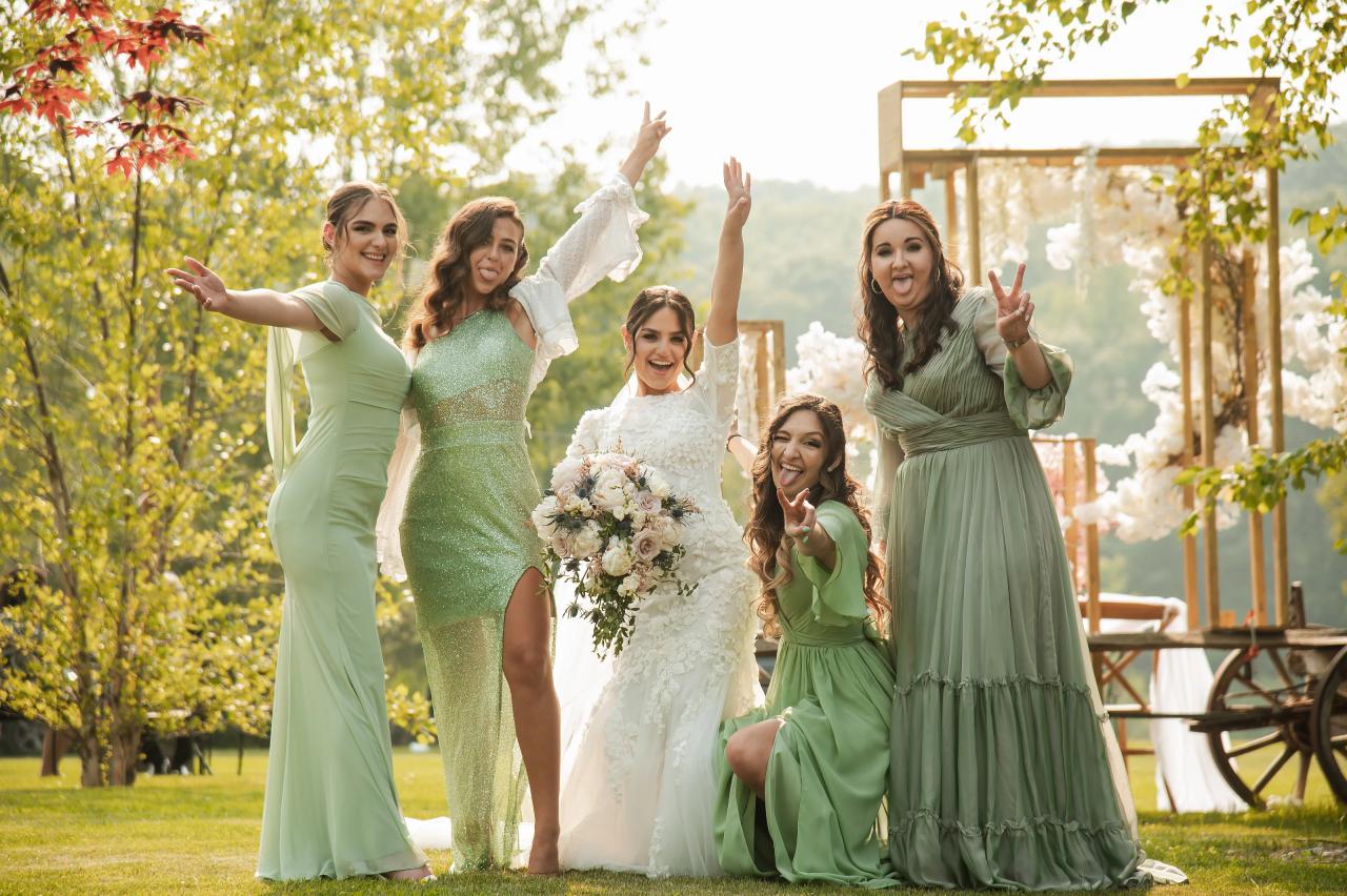 Smiling wedding party celebrates outdoors in warm sunlight as the bride walks forward with bouquet, arms raised and dresses flowing. Wedding photography at The Barn At Indian Ridge, Highland, NY.