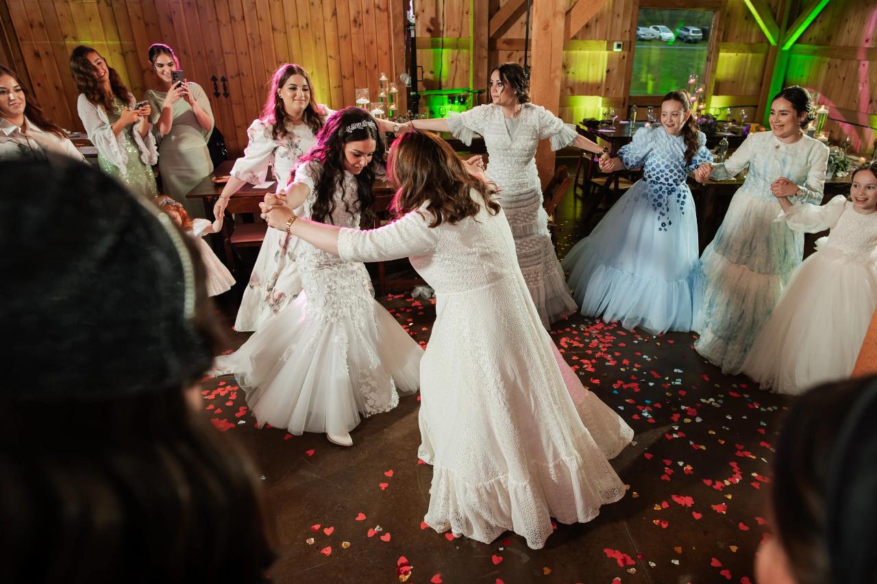 Bride dancing in a wood-paneled hall with green uplighting as confetti hearts scatter across the floor and guests clap from both sides. Wedding photography at The Barn At Indian Ridge, Highland, NY.
