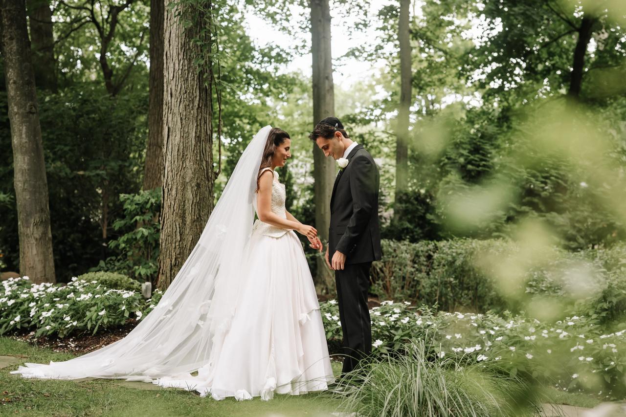 Bride and groom standing close and holding hands in a garden walkway, with the bride’s veil flowing and soft greenery bokeh in the foreground. Wedding photography at Crystal Plaza, Livingston, NJ.