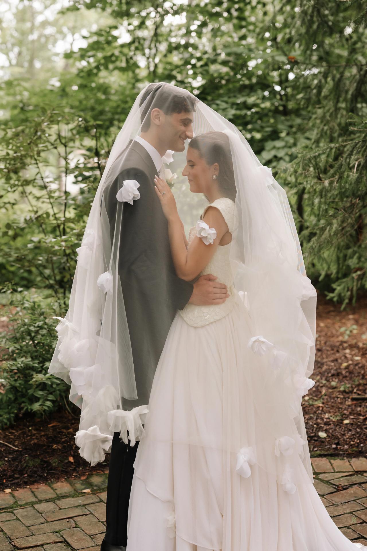 Bride and groom sharing an intimate moment outdoors, the bride’s veil framing their faces as they hold each other’s hands and smile softly. Wedding photography at Crystal Plaza, Livingston, NJ.