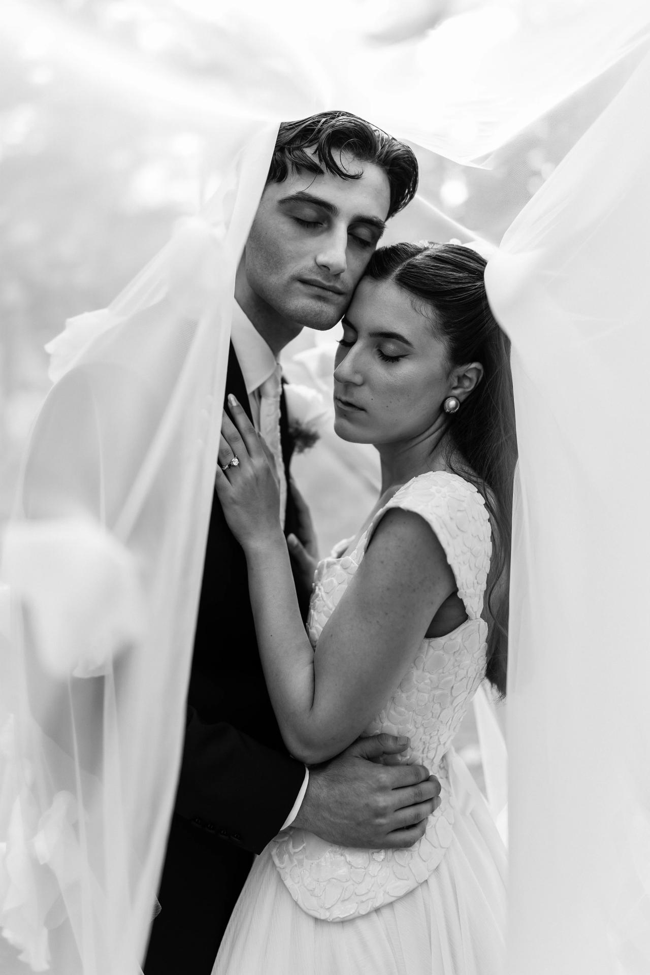 Black-and-white close-up of a bride and groom embracing as the groom leans in under a veil, faces near and eyes closed. Wedding photography at Crystal Plaza, Livingston, NJ.