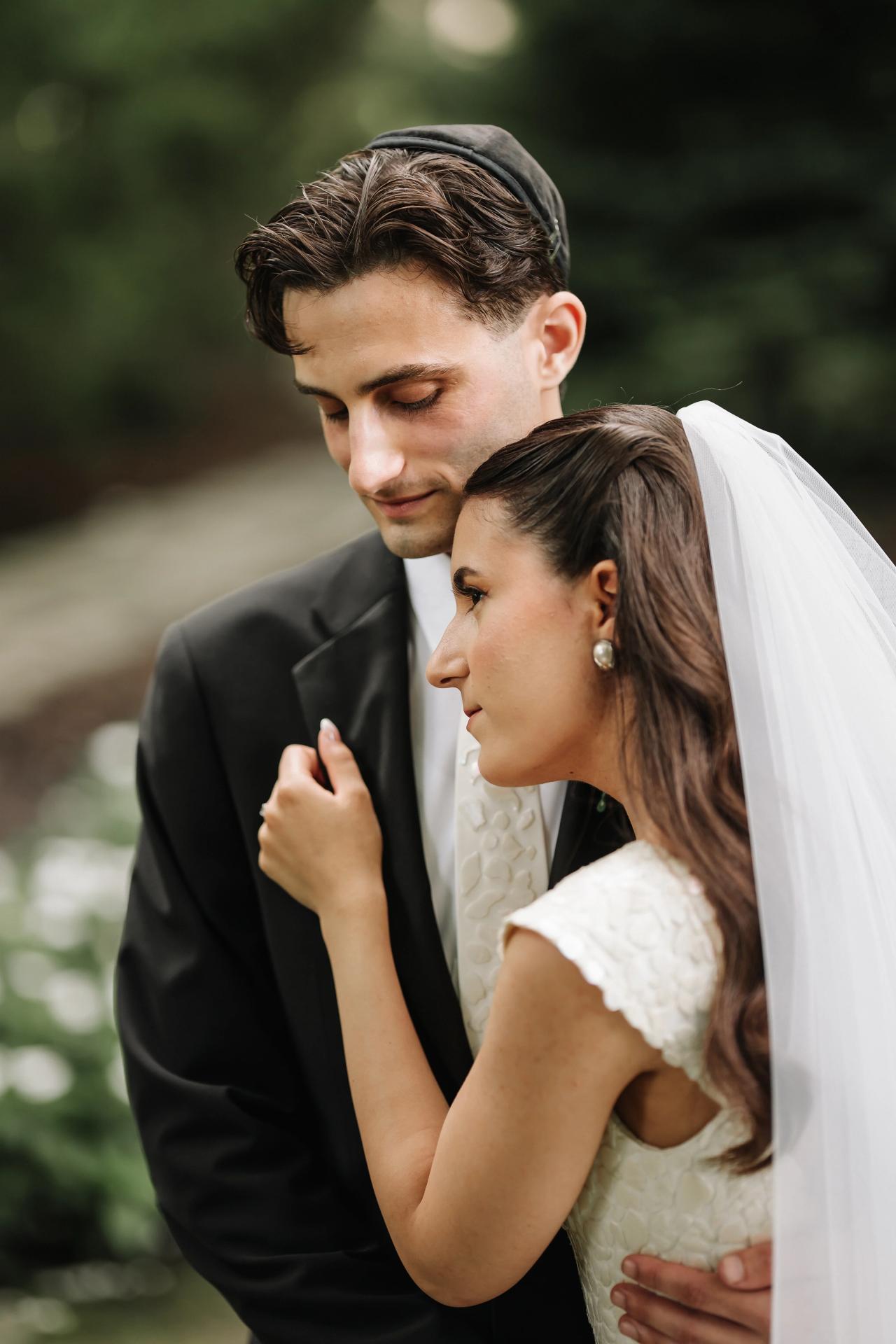 Outdoor wedding portrait of a bride and groom embracing closely, faces turned toward each other with soft background blur and warm tones. Wedding photography at Crystal Plaza, Livingston, NJ.