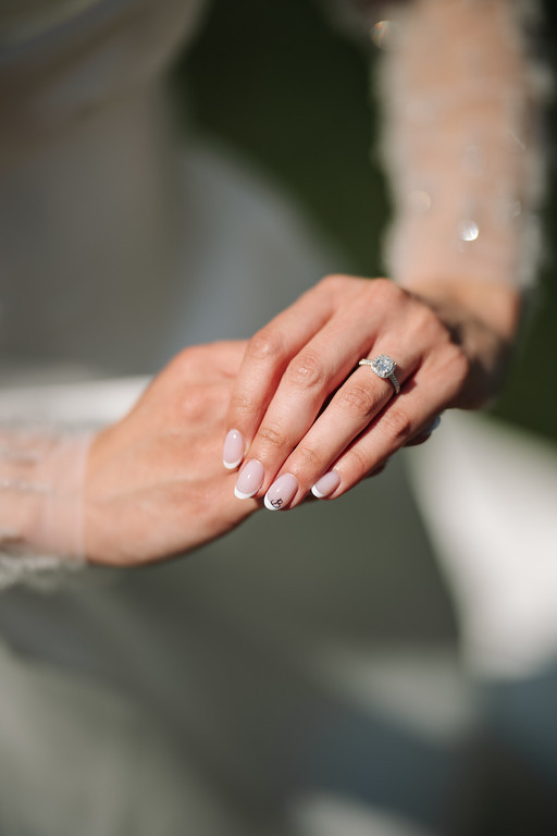 Close-up of two hands clasped together, showing an engagement ring and manicured nails.