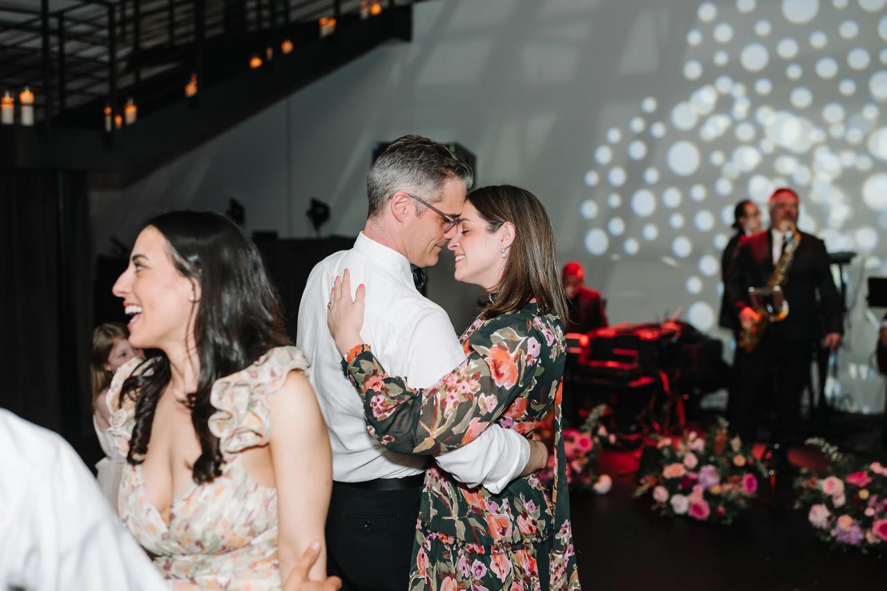 Couple hugging and smiling at each other on a lit dance floor during a wedding reception, with stage and bokeh lights in the background.