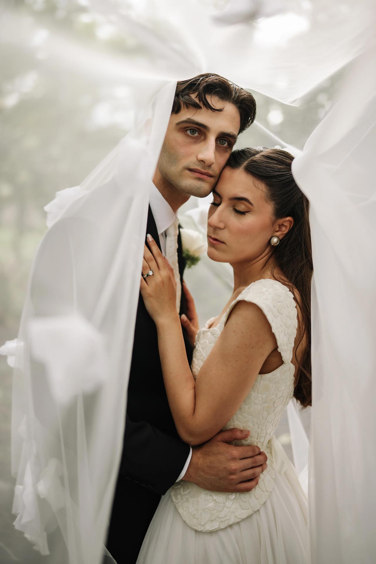 Bride and groom in a close embrace during badeken, veil draped over the bride, soft bright light and intimate expressions. Wedding photography at Crystal Plaza, Livingston, NJ.