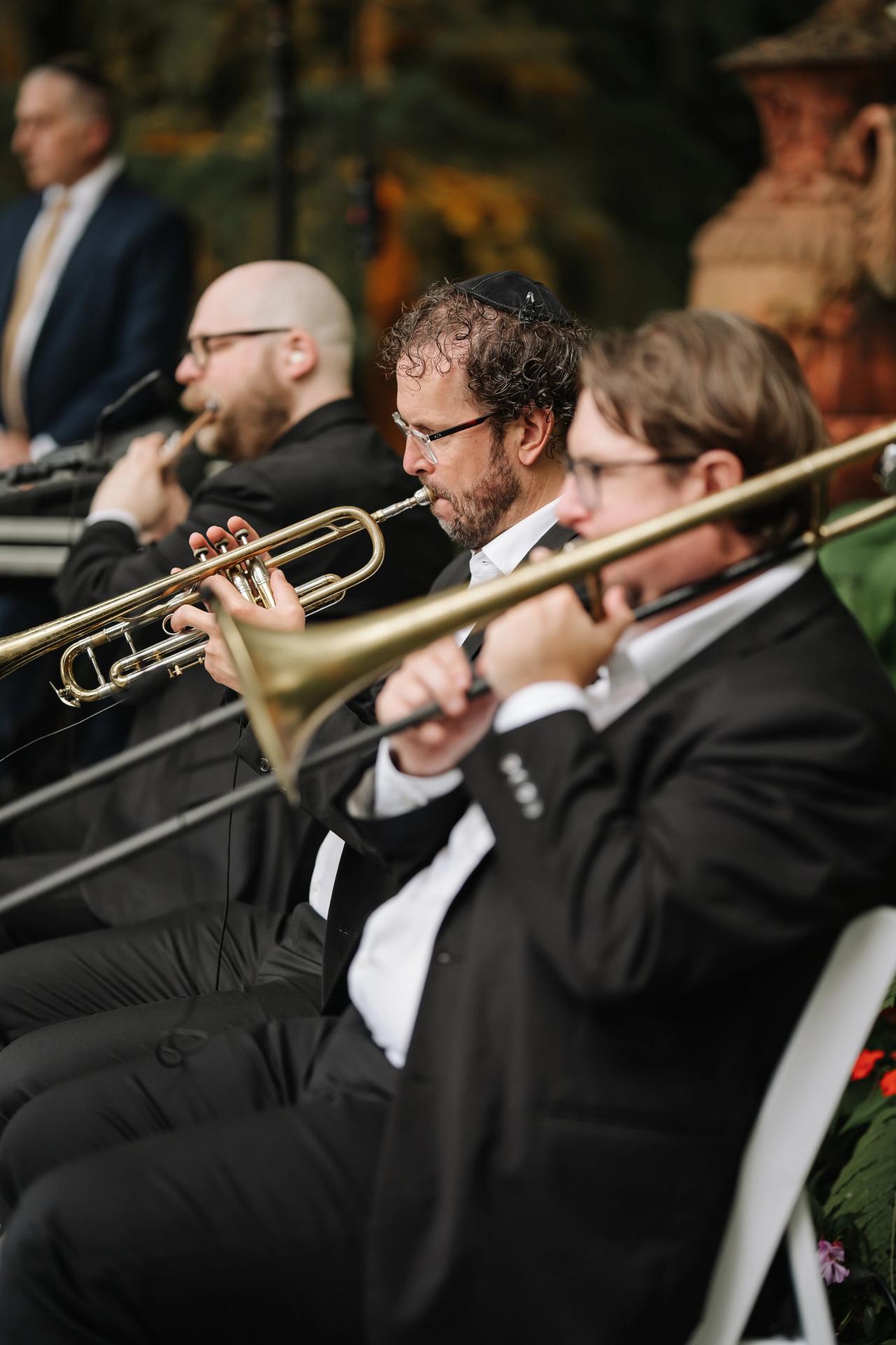 Close-up of a trumpet player in a wedding band performing, with other musicians softly blurred in the background. Wedding photography at Crystal Plaza, Livingston, NJ.