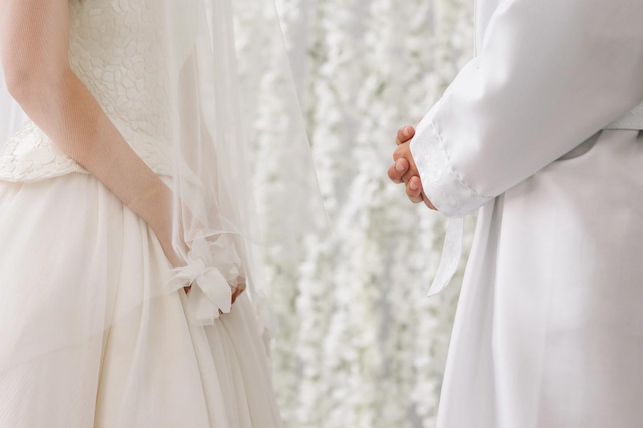 Close-up of a bride and groom holding hands, framed by their white wedding attire and soft, light background. Wedding photography at Crystal Plaza, Livingston, NJ.