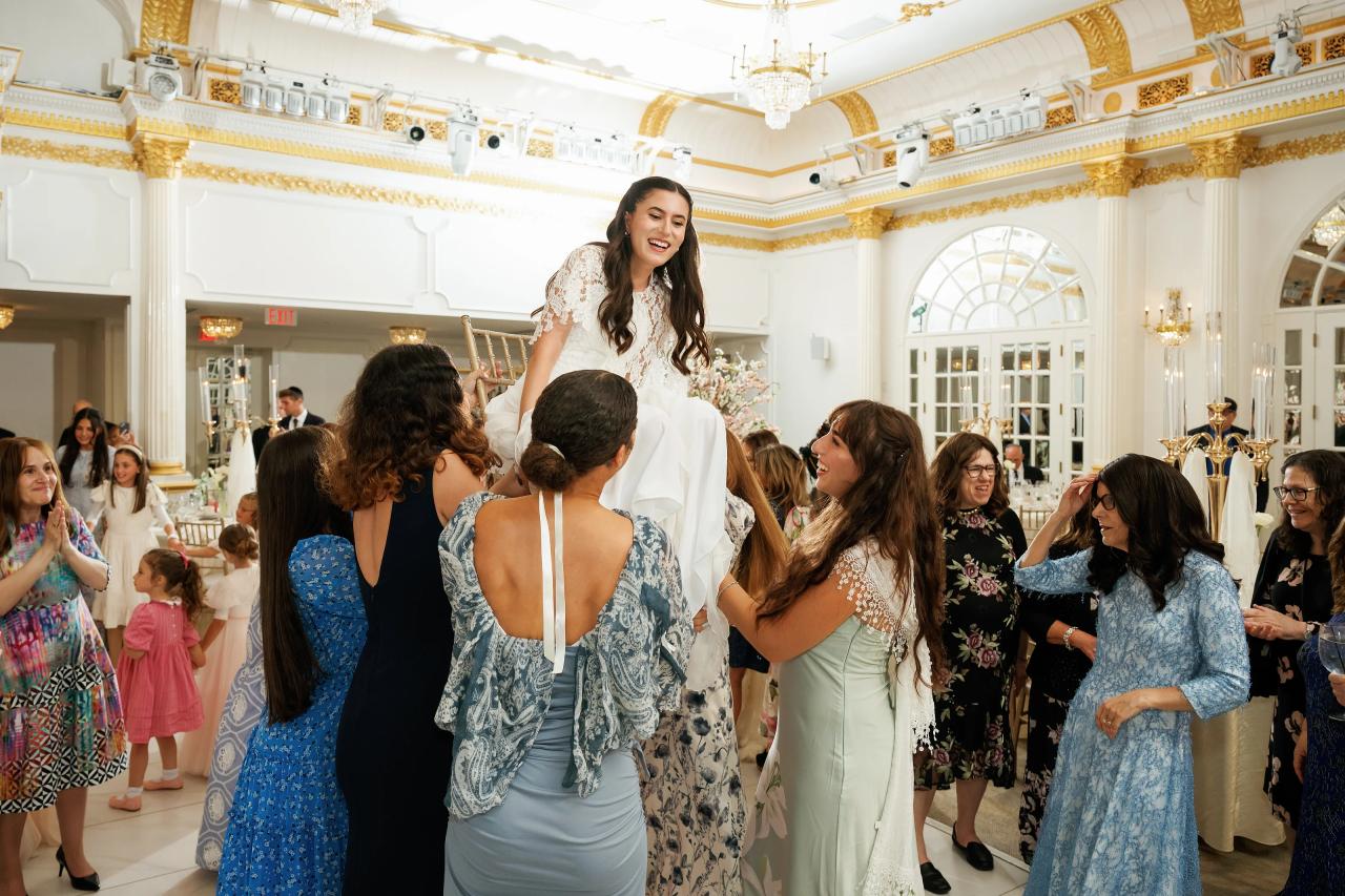 Bride laughing joyfully as guests surround and clap during a reception dance-floor moment in an elegant white-and-gold hall. Wedding photography at Crystal Plaza, Livingston, NJ.