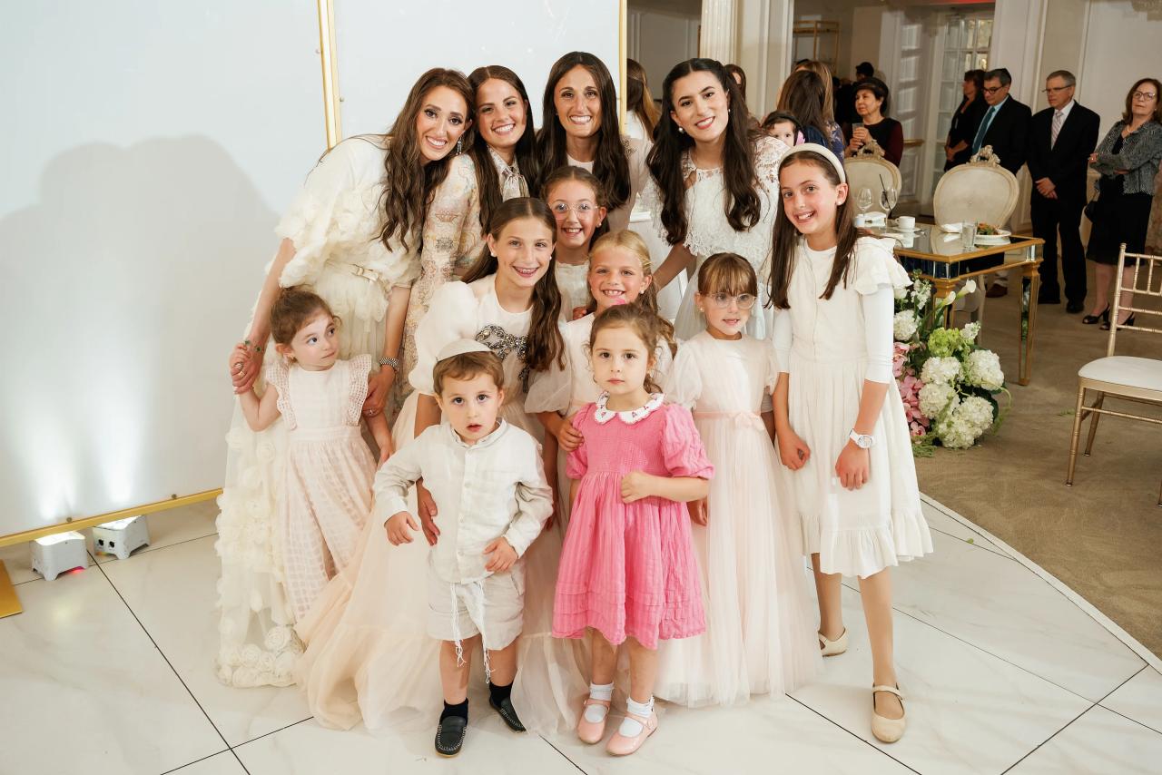 Posed group photo of close family and children at a bright indoor reception space, wearing coordinated white and occasion outfits. Wedding photography at Crystal Plaza, Livingston, NJ.
