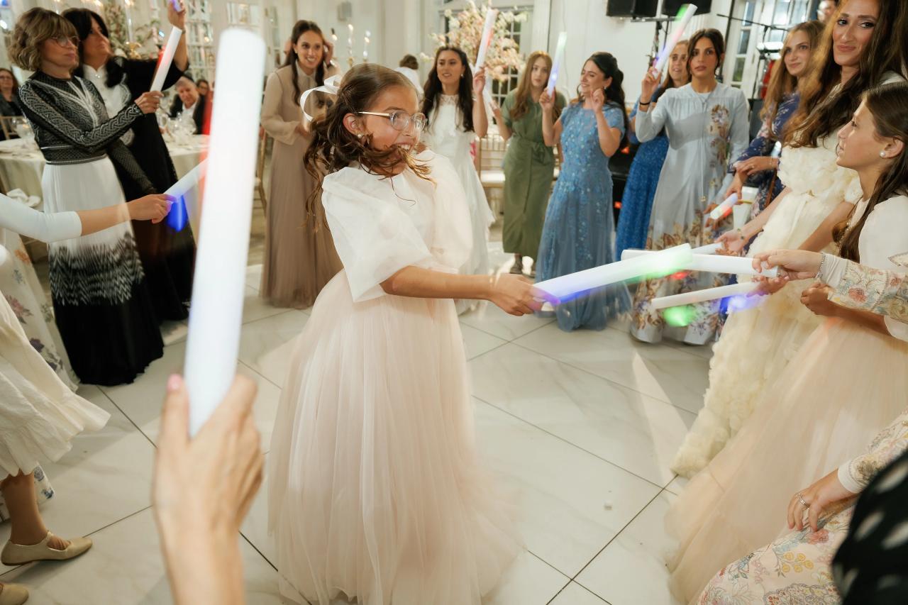 Frum wedding bride dancing forward in a brightly lit indoor hall as guests cheer along both sides with illuminated light sticks. Wedding photography at Crystal Plaza, Livingston, NJ.