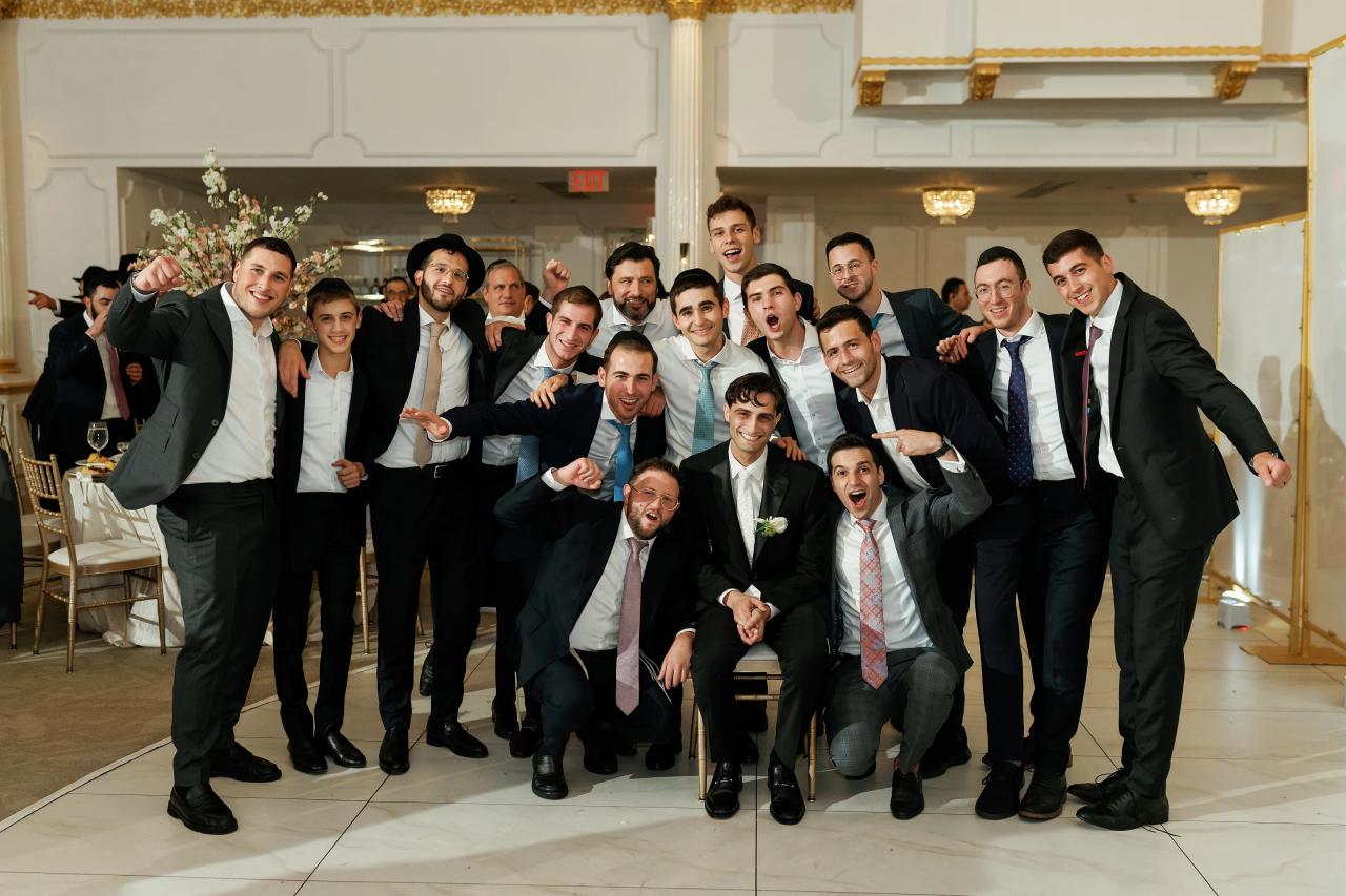 Wedding reception group photo of many guests in formal attire cheering and smiling indoors, framed by banquet hall décor and warm lighting. Wedding photography at Crystal Plaza, Livingston, NJ.