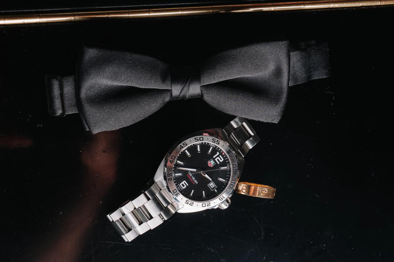 Close-up of a silver wristwatch with a black bow tie and small cuff detail on a dark surface. Wedding photography at Tribeca Rooftop + 360°, New York, NY.