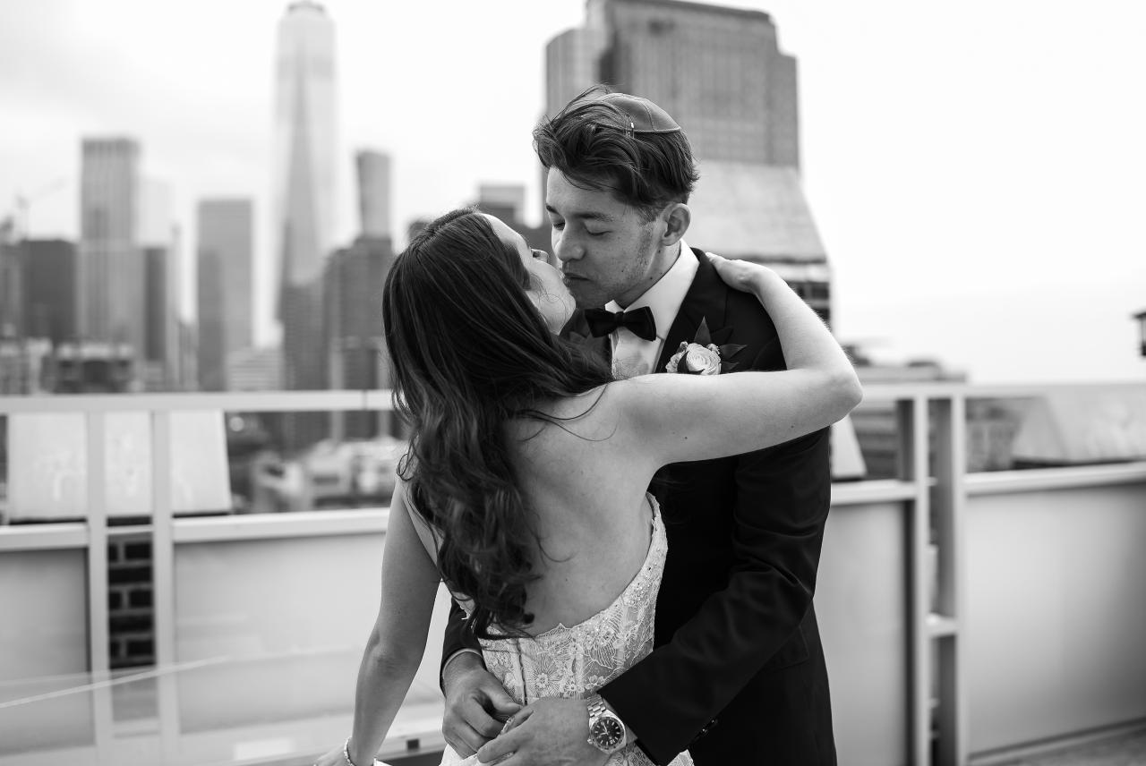 Black-and-white rooftop portrait of a bride and groom embracing closely, facing each other in an intimate moment with the city skyline blurred in the background. Wedding photography at Tribeca Rooftop + 360°, New York, NY.