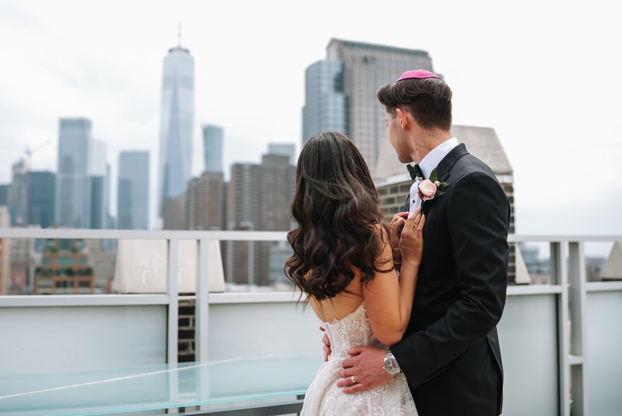 Bride and groom in a tender embrace on a rooftop, with a bright city skyline in the background. Wedding photography at Tribeca Rooftop + 360°, New York, NY.
